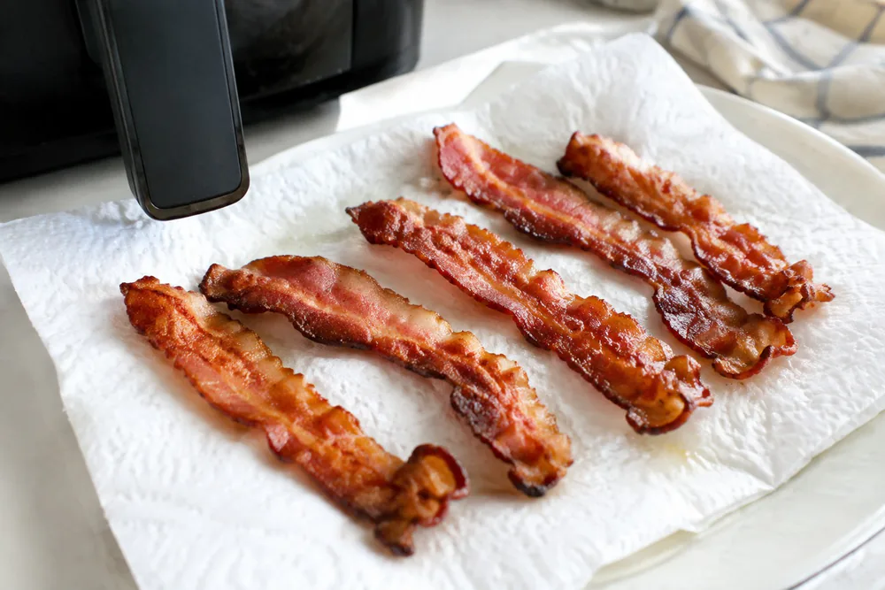 Crispy bacon strips on paper towels after air frying.
