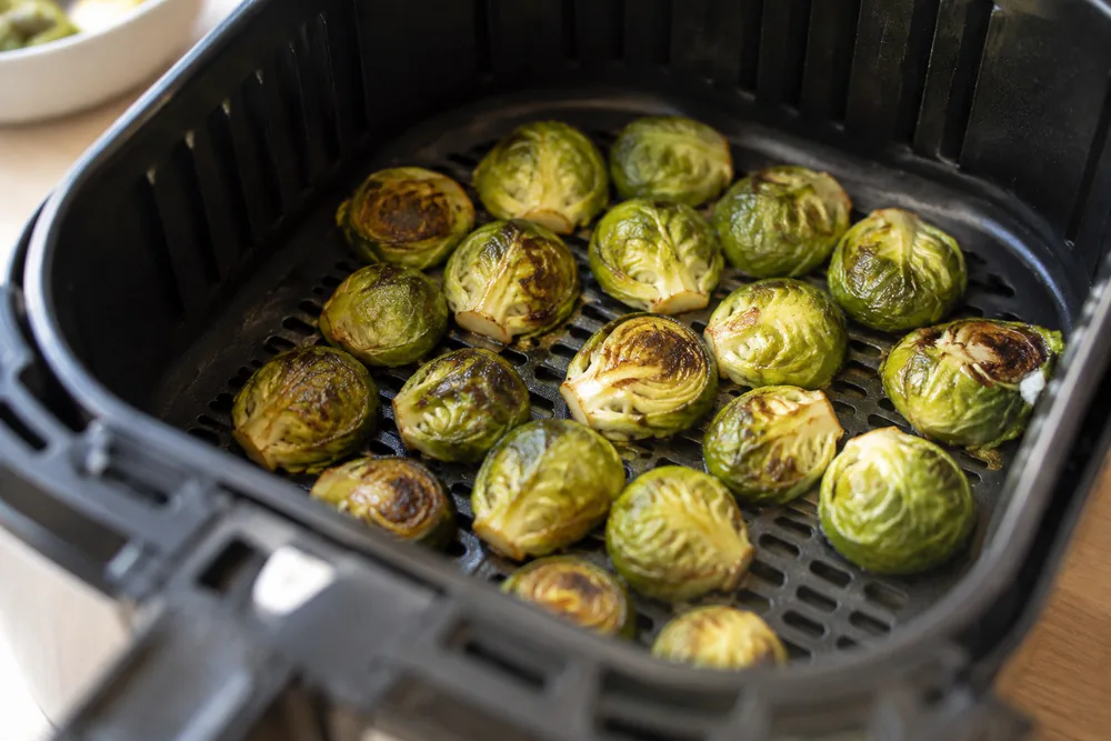 Halved brussels sprouts cut side down in an air fryer basket.