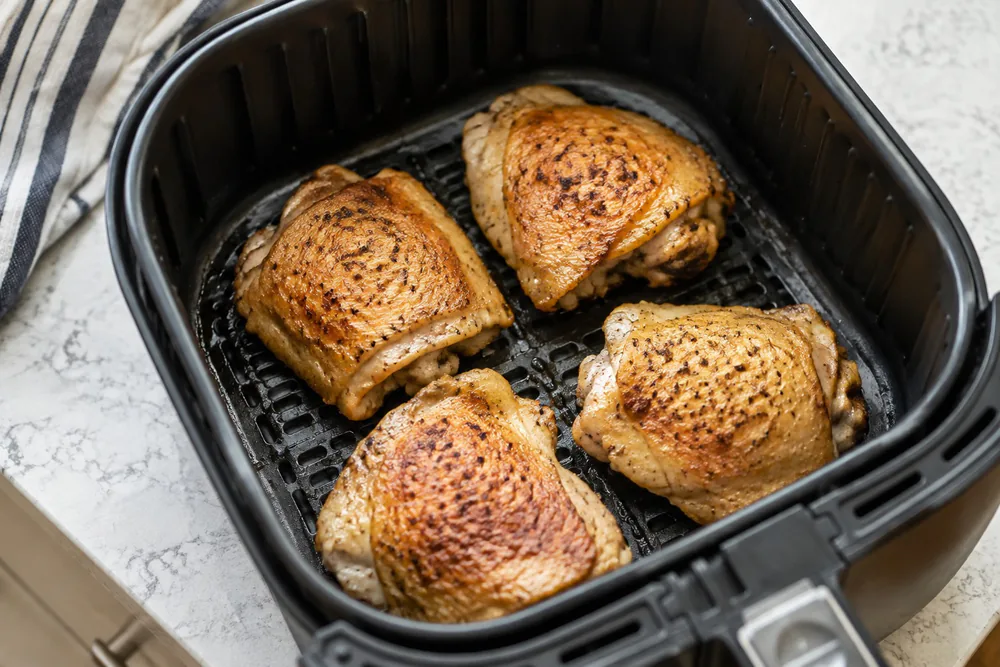 Bone-in chicken thighs skin side up in an air fryer basket.