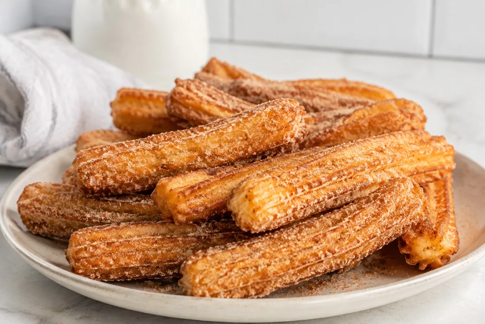 Cinnamon sugar churros piled on a plate.
