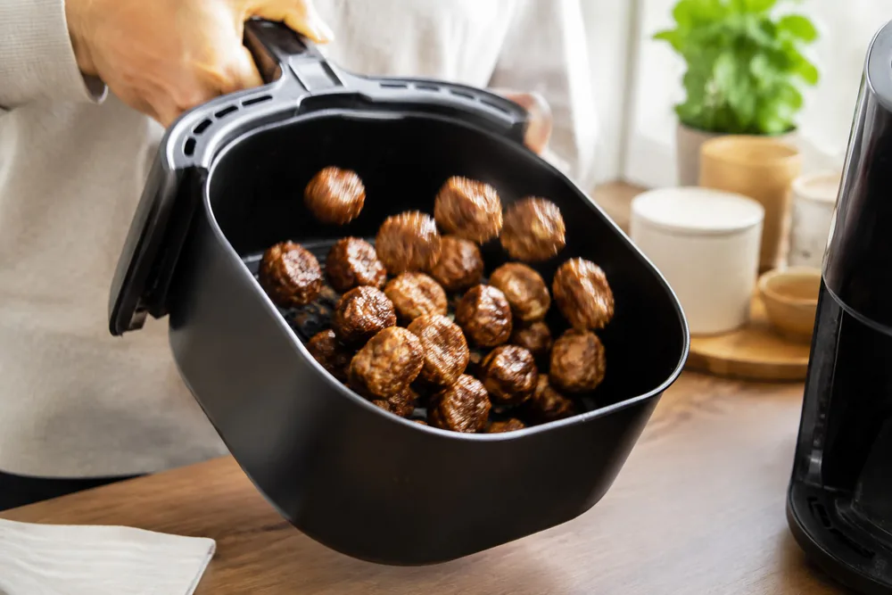 Small meatballs shaking in an air fryer basket.