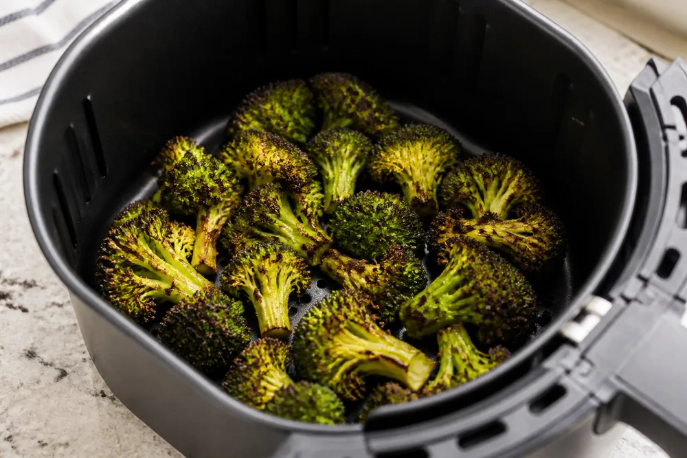 Charred broccoli florets with crispy edges in an air fryer basket.