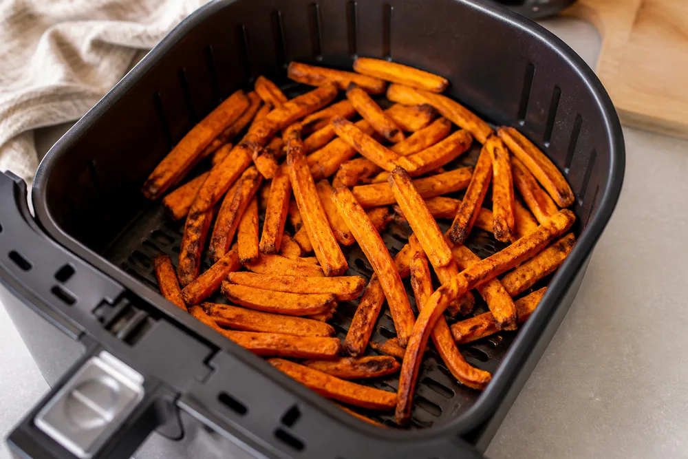 Sweet potato fries with charred edges in an air fryer basket.