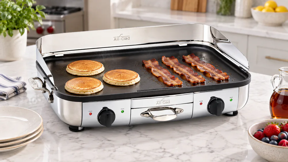 Pancakes cooking on one half of the All-Clad 99014GT griddle while bacon sizzles on the other half, showing the two temperature zones