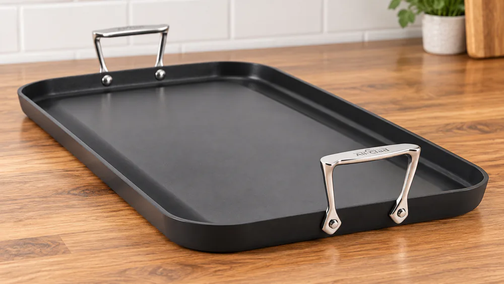 All-Clad HA1 double burner griddle showing its riveted stainless steel handle, black hard-anodized body and nonstick cooking surface on a countertop