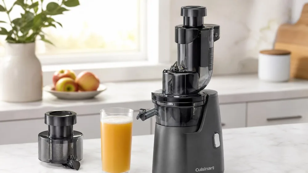A glass of apple juice from the Cuisinart CSJ-300 with a thin foam layer on top, the mesh-free filter nearby.