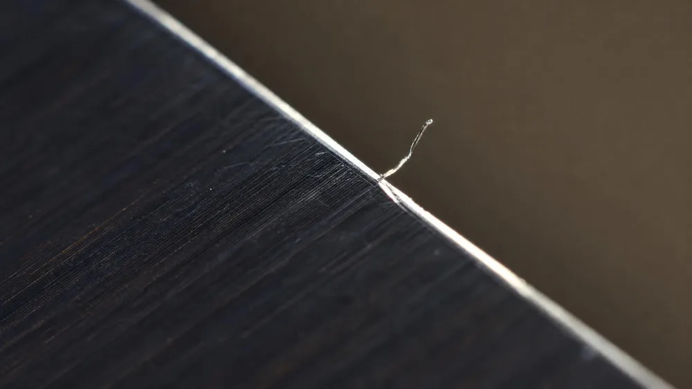 A close-up of a burr formed along a knife edge during sharpening, a thin wire of steel catching the light.