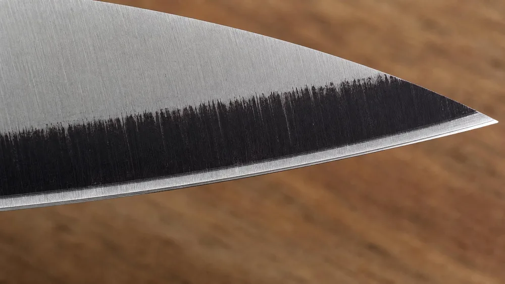 A knife bevel coated in permanent marker after a single whetstone stroke, ink cleared from shoulder to apex where the angle matches.