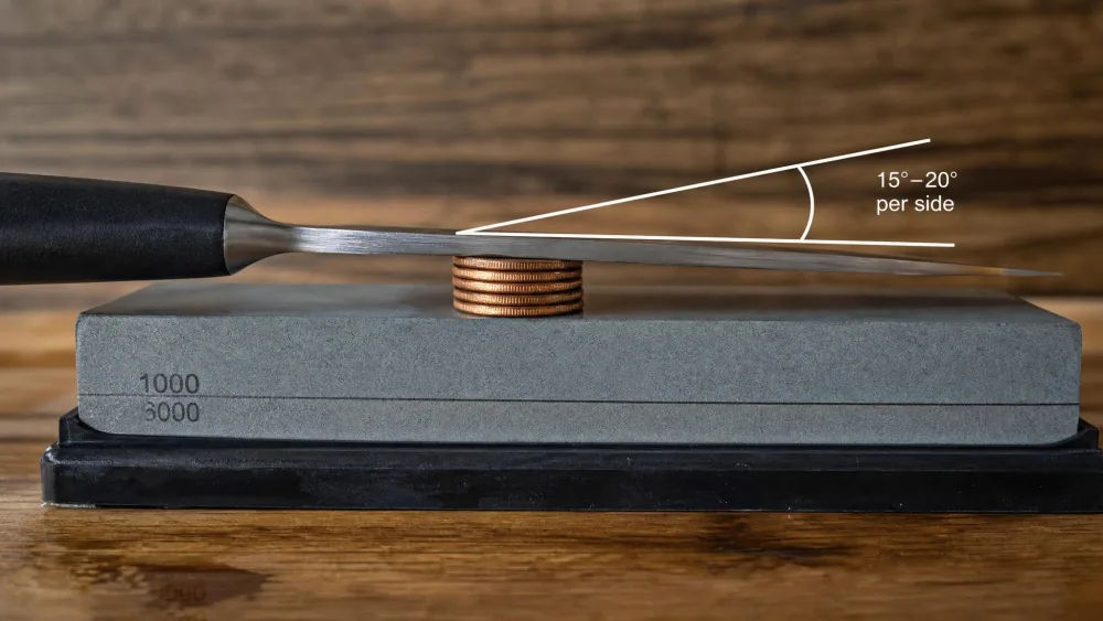 Pennies stacked under a knife spine on a whetstone to set a 15 to 20 degree per side freehand sharpening angle.