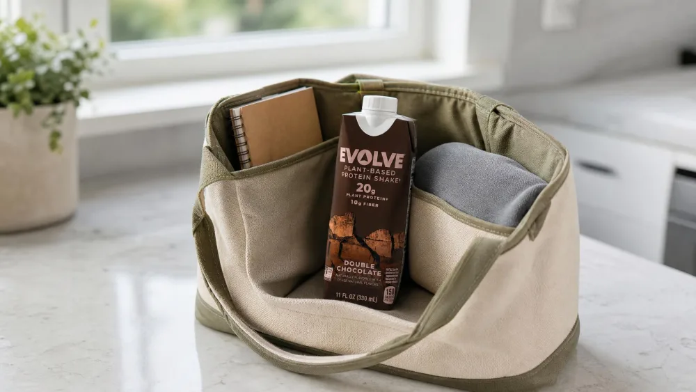 An Evolve Double Chocolate bottle standing upright in a work tote alongside a notebook, packed for the day.