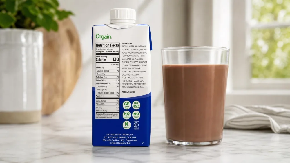An Orgain Clean Grass Fed chocolate bottle turned to show its short ingredient list beside a glass of the poured shake.