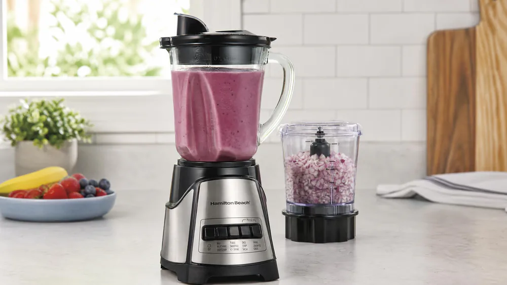 A Hamilton Beach Power Elite glass jar of smoothie on a counter, with the mini chopper behind it.