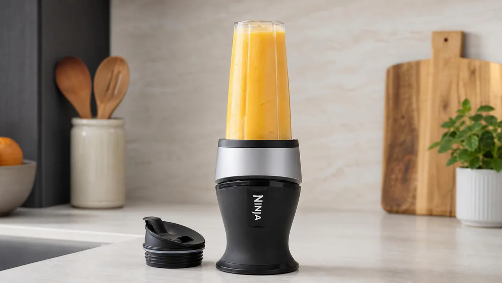 A Ninja Fit personal blender with a 16 oz cup of frozen mango drink, spout lid next to it on the counter.