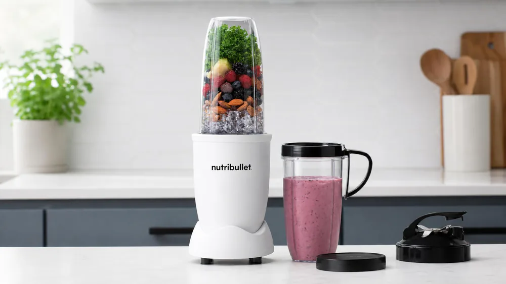 A NutriBullet Pro 900 with a 32-ounce cup of berry smoothie, the blade base twisted off and resting beside it.