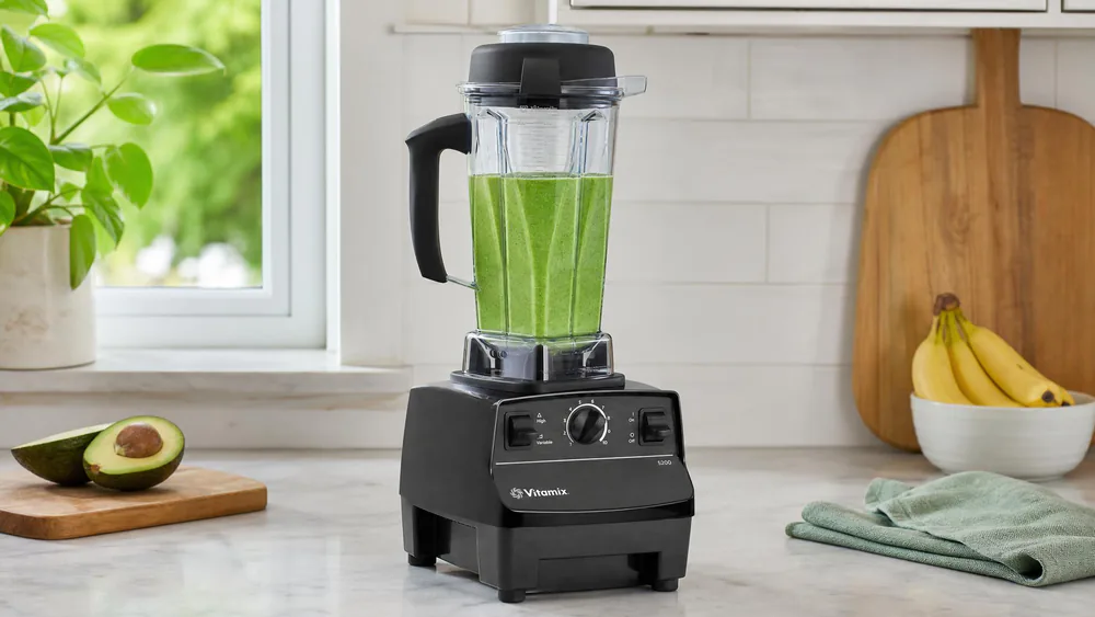 A Vitamix 5200 on a kitchen counter with the tall 64-ounce classic jar filled with a green smoothie, the dial set to high.