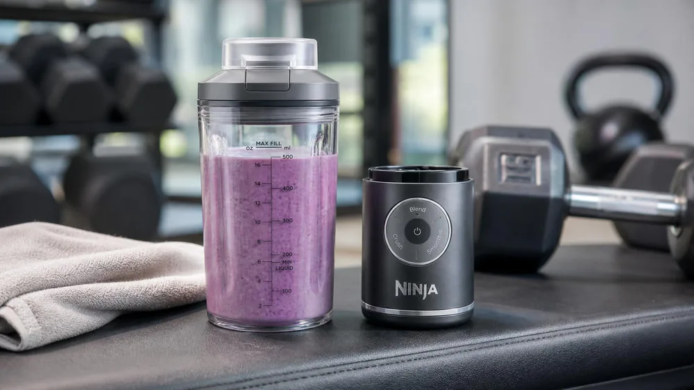 The Ninja Blast Max with its 22-oz Twist & Go vessel detached from the motor base on a gym bench, shake blended and lid on.