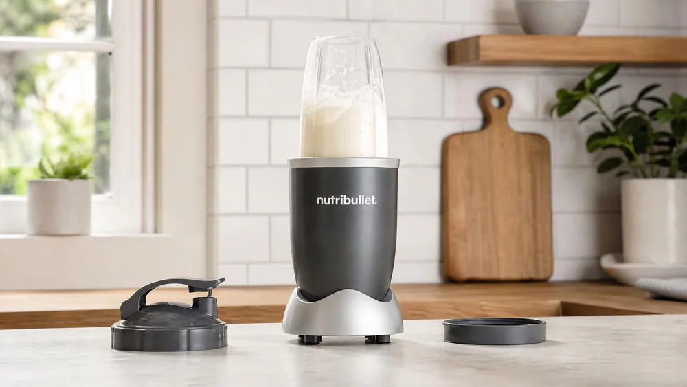 A NutriBullet 600 with its 24-oz cup threaded onto the motor base mid-blend on a kitchen counter, milk and whey swirling in the cup.