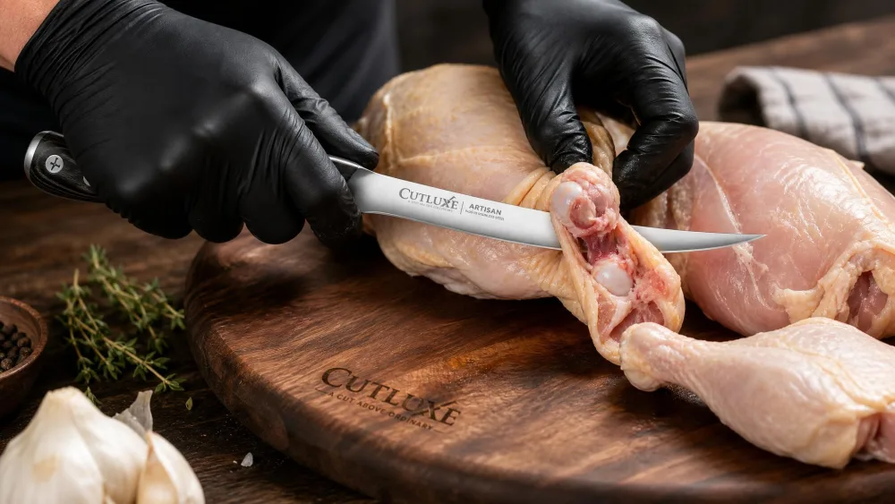 A Cutluxe curved boning knife with a pakkawood handle working around chicken joints on a board.