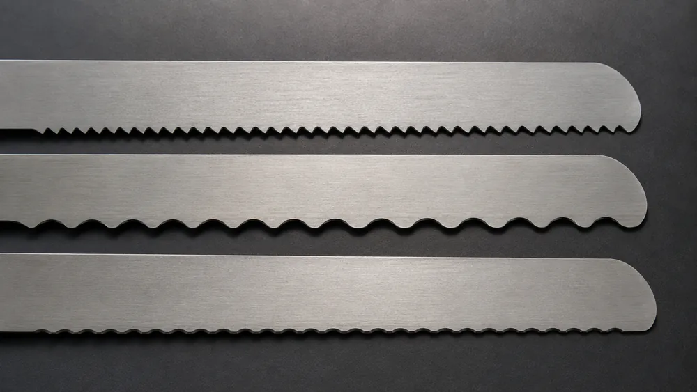 Close-up of pointed, scalloped, and wavy serration patterns on three bread knife edges side by side for comparison.