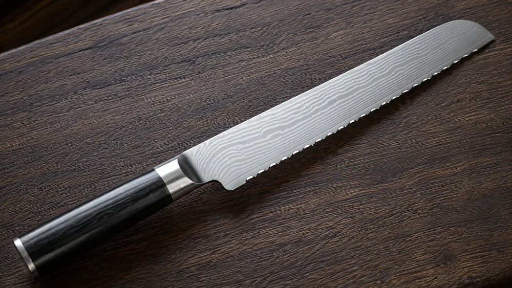 Close-up of the Shun Classic 9-inch serrated edge showing the Damascus cladding pattern rippling across the blade face.