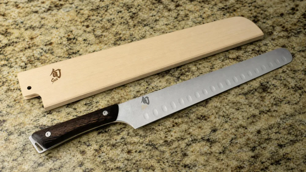 The Shun Kanso 12-inch brisket knife beside its wooden saya sheath, tagayasan handle visible.