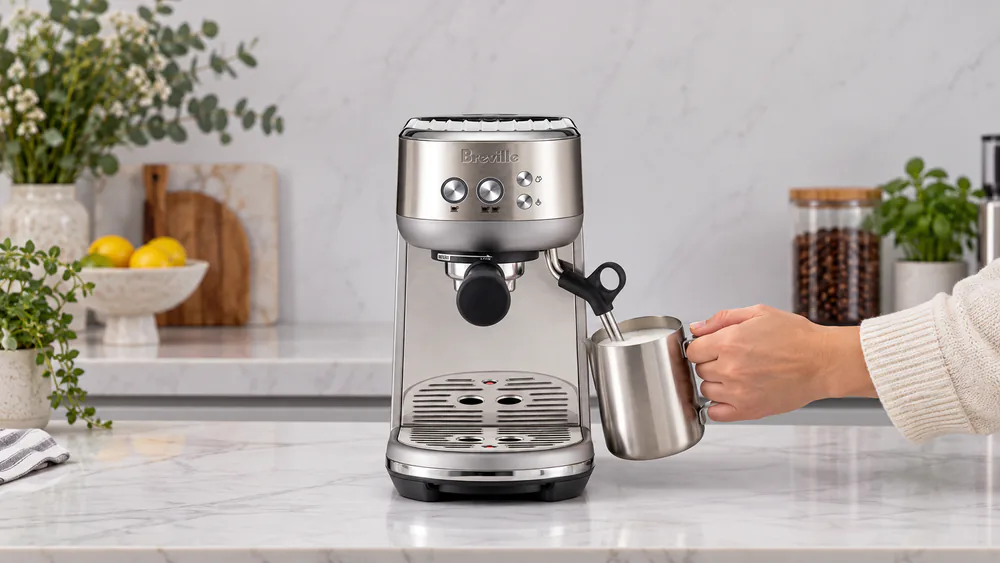 Breville Bambino manual steam wand texturing milk in a stainless pitcher on a small kitchen counter