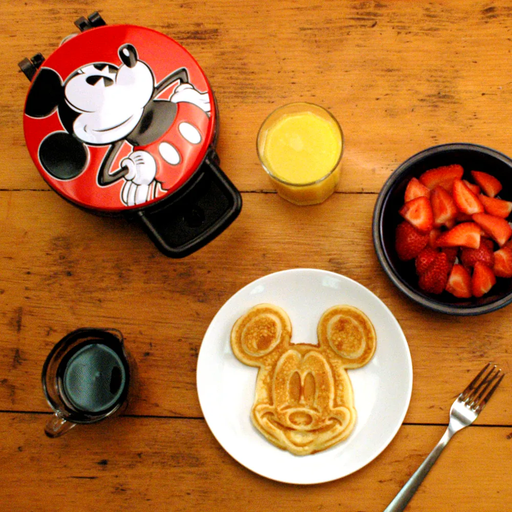 Manufacturer breakfast photo of the red Mickey Mouse waffle maker beside a Mickey-shaped waffle, strawberries and orange juice