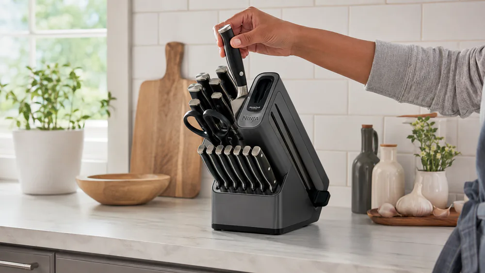 A hand pulling a knife from the Ninja Foodi NeverDull block while the block's suction cups hold it on the counter.