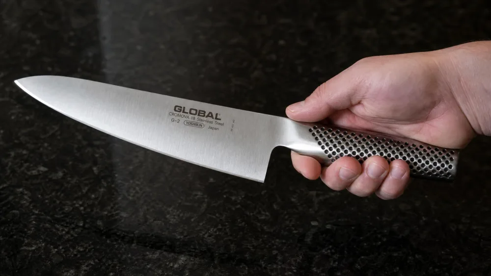 The all-steel Global G-2 held handle-forward, the dimpled grip pattern catching the light against a dark countertop.