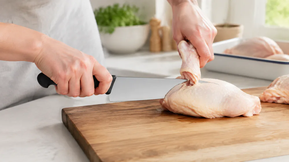 The Victorinox Fibrox Pro blade flexing slightly under lateral pressure against a chicken leg joint during the butchering test.