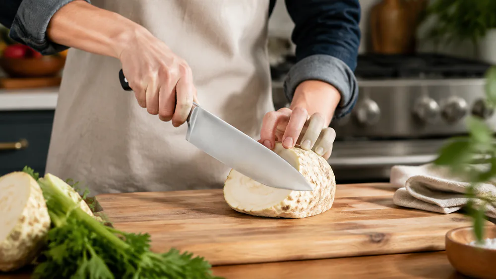 The Wüsthof Classic cutting through a dense celery root half on a cutting board, weight doing the work.