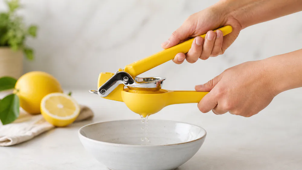 Hands squeezing a lemon half in a Chef'n FreshForce handheld citrus squeezer over a bowl, juice running through the hinged cup.