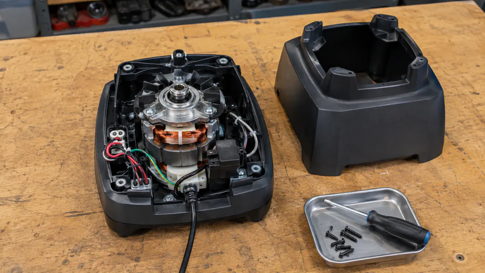 A commercial blender base opened up on a workbench showing the motor, wiring, and drive coupling during our durability inspection.