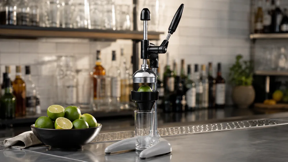 A Hamilton Beach Commercial 932 on a bar counter beside a stack of limes and a pint glass under its spout.