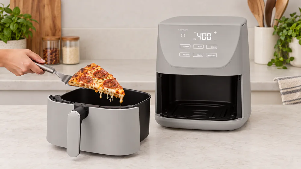 A reheated pizza slice with melted cheese and a crisp crust lifted from the basket of a light gray CruxGG 6QT air fryer