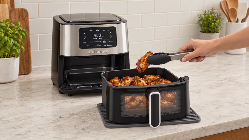 A batch of chicken wings being lifted from a Cuisinart air fryer basket during a crisping test, skin browned and rendered.