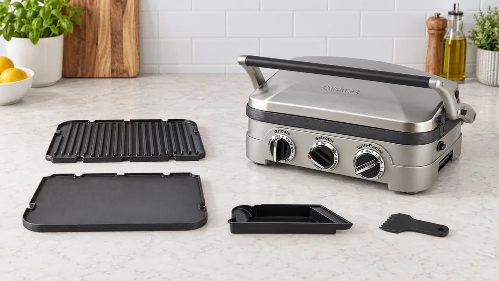 Two removable Cuisinart Griddler nonstick plates lifted out of the base and set on a kitchen counter next to the drip tray and scraper