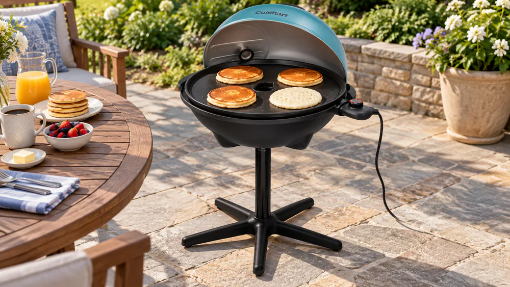 The Cuisinart Indoor/Outdoor electric griddle on its stand on a patio with a row of pancakes cooking on the flat nonstick surface