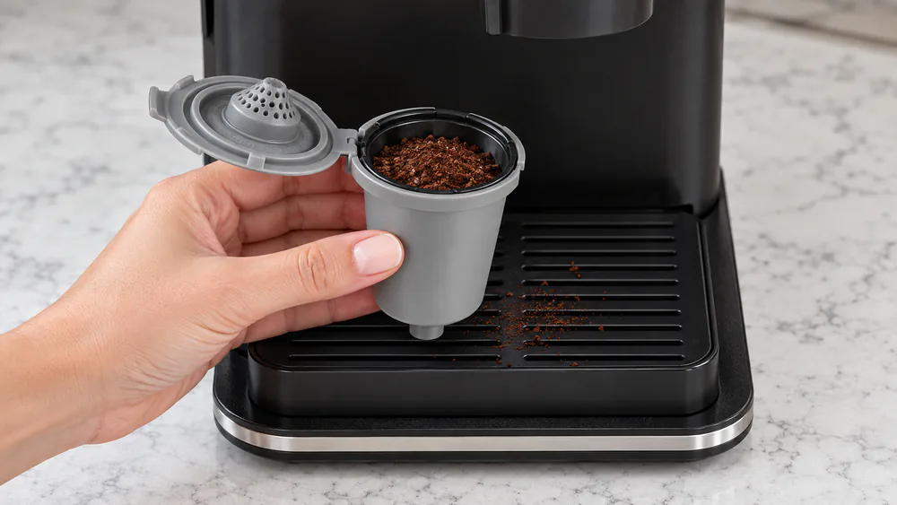 The HomeBarista reusable filter cup of a Cuisinart DGB-2 filled with fresh medium-fine grounds, a few spilled grounds visible on the tray below