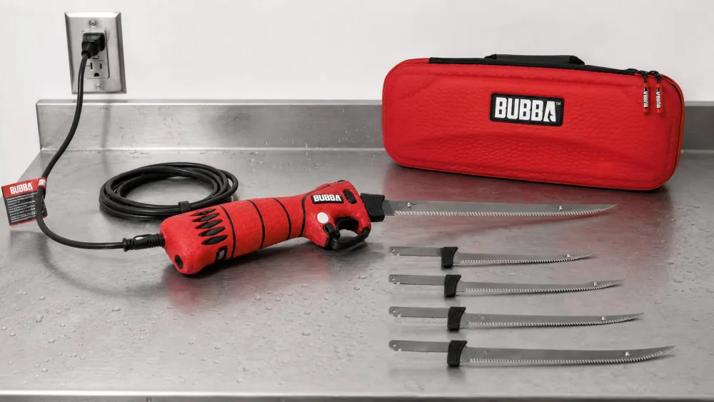 The BUBBA 110V corded electric fillet knife on a cleaning table, its 8-foot power cord trailing to an outlet, four blades laid out beside it.