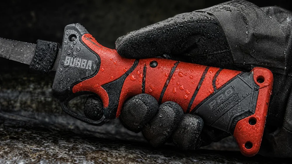 The BUBBA Pro lithium-ion handle held in a gloved hand, tacky rubber grip and trigger guard visible, fish slime beading on the surface.