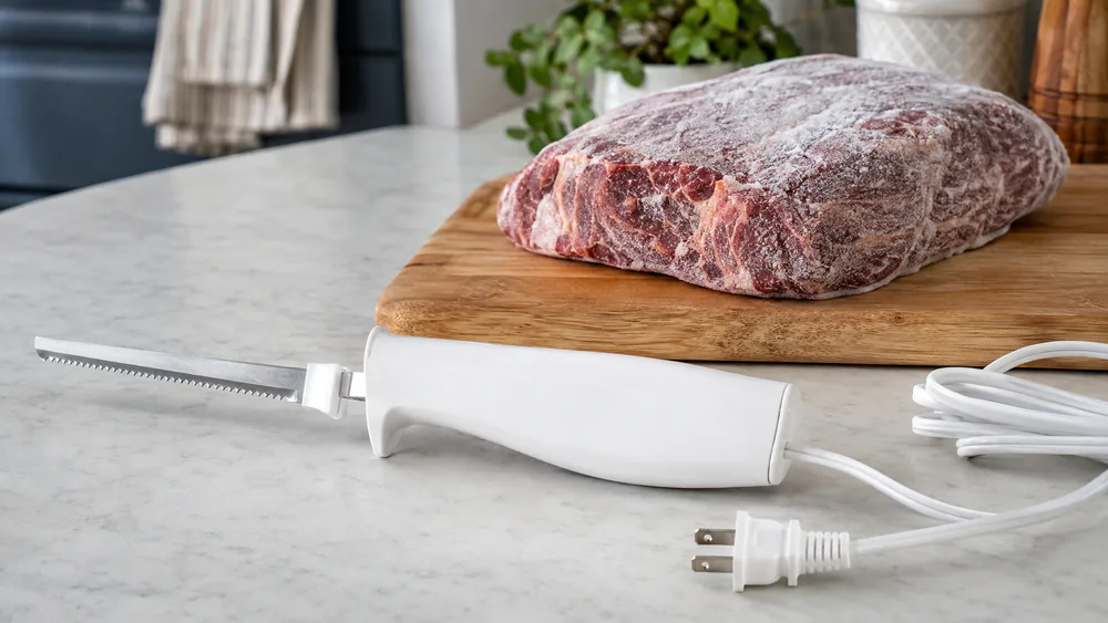 An electric knife set down beside a still-frozen roast on a cutting board.