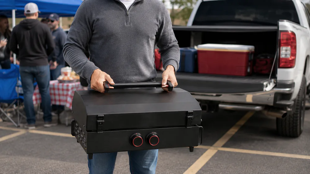 A Camp Chef Gridiron Gameday 24 portable griddle latched shut with its legs folded, carried like a case at a tailgate.