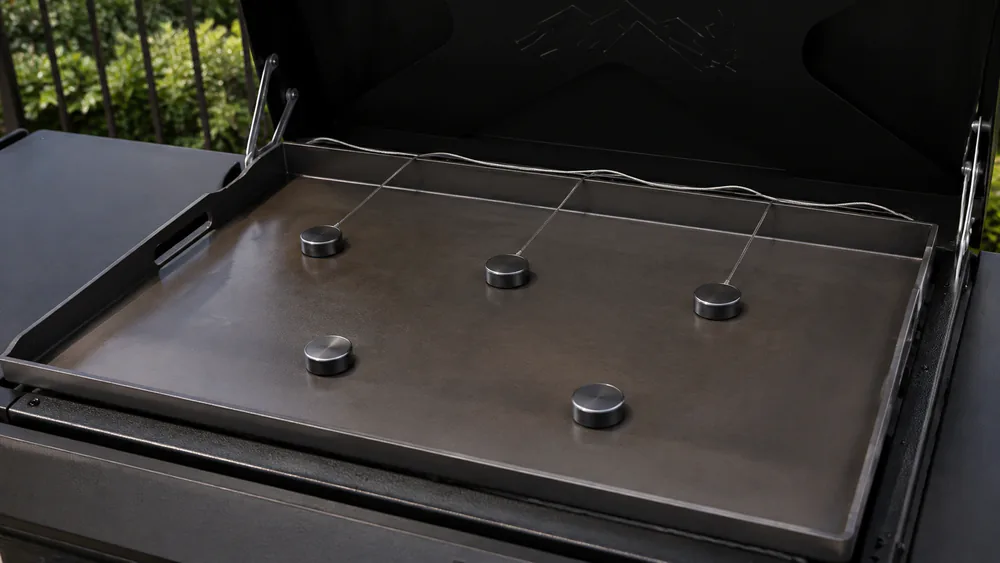 A flat top grill cooktop with surface temperature probes laid across the cooking area during a heat evenness test.