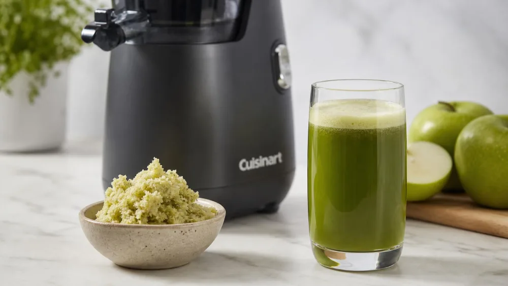 A scoop of crumbly bone-dry apple pulp from the Cuisinart CSJ-300 slow juicer next to a glass of apple juice with a thin foam cap