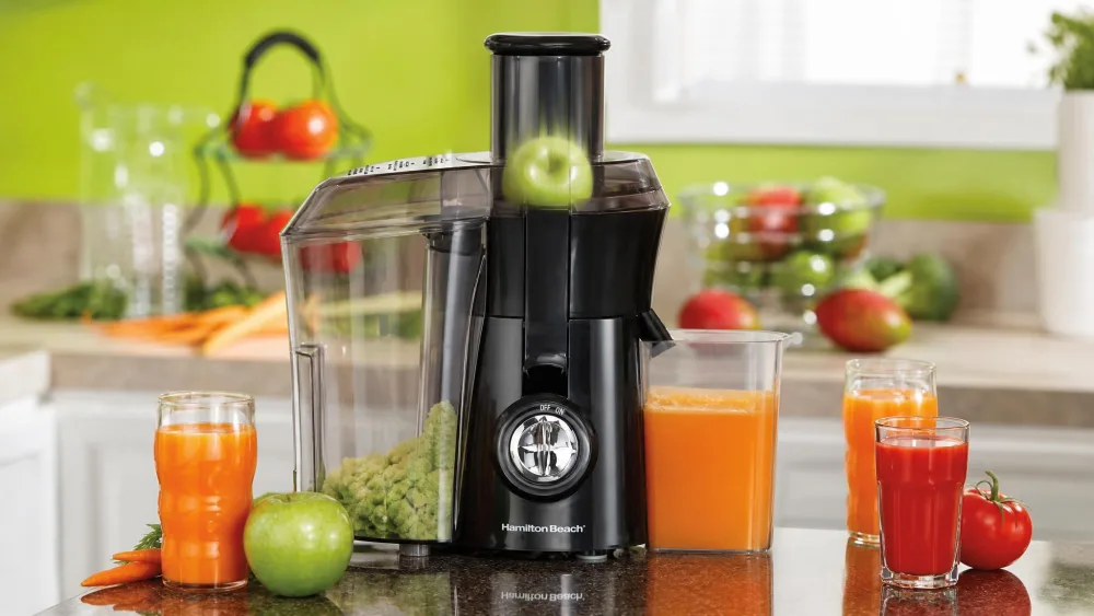 A whole apple disappearing into the 3-inch Big Mouth chute of the Hamilton Beach 67601A juice extractor, pulp bin attached, motor running