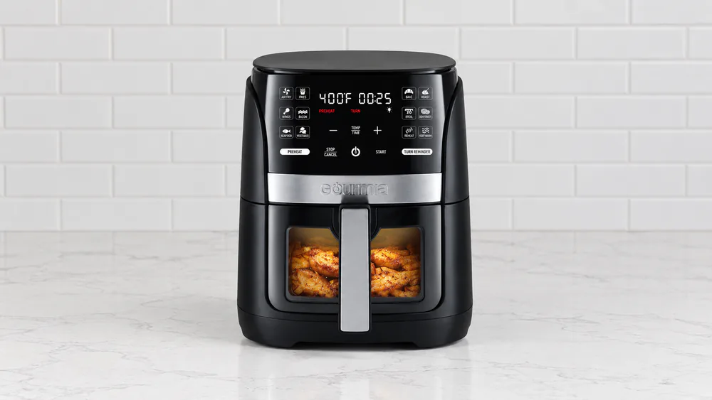 A Gourmia GAF616 window air fryer with the interior light on, chicken wings browning visibly through the glass