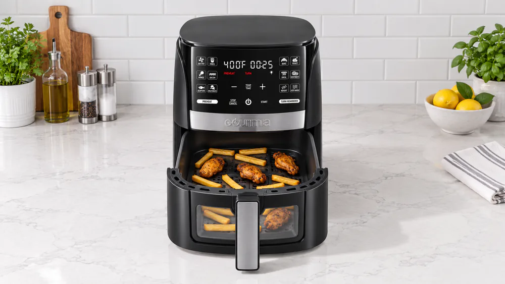 A Gourmia 6 quart air fryer basket pulled halfway out, filled with frozen fries and chicken wings in a single layer on a kitchen counter