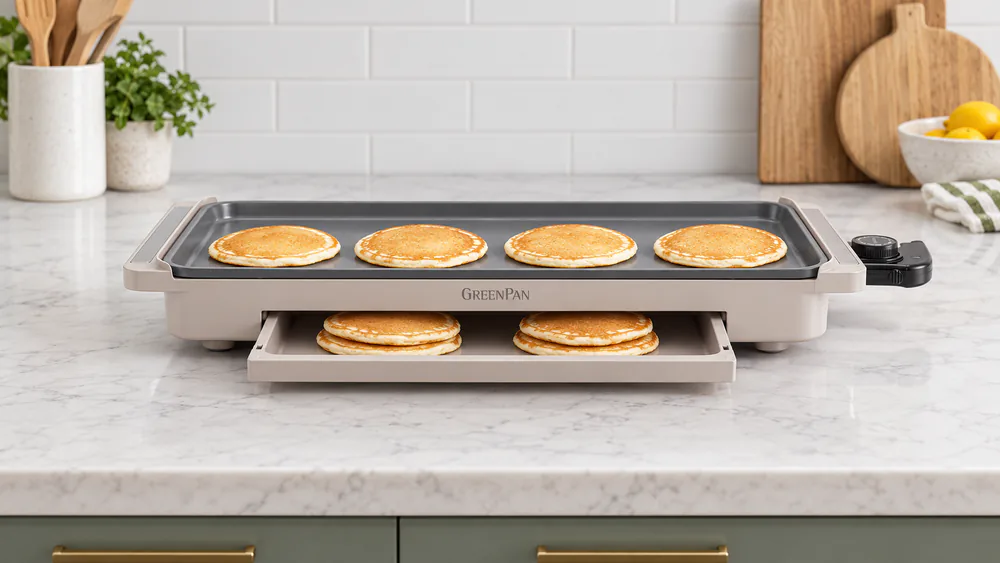 The GreenPan Advanced griddle with its warming drawer pulled open and a stack of pancakes inside while a fresh batch cooks on top