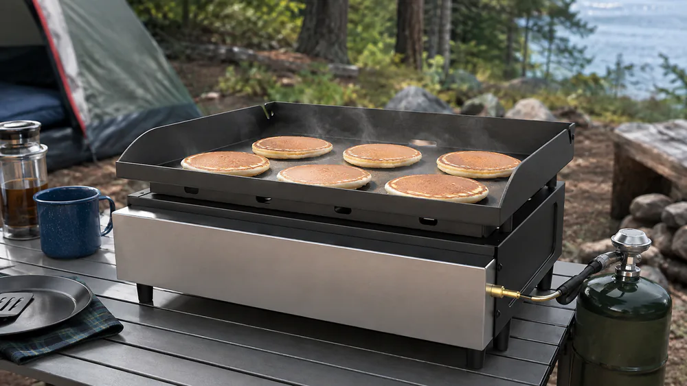 The Blackstone 22-Inch Tabletop Griddle on a camp table, pancakes cooking on its rolled carbon steel surface.